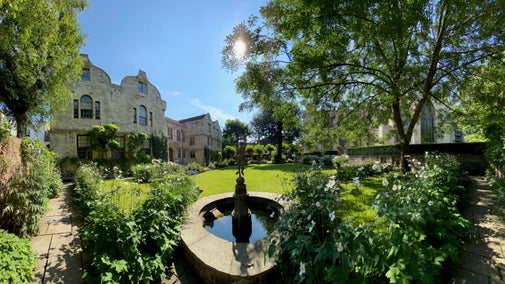 View on a sunny day with a fountain stature in the foreground and lawn, trees and blue sky beyond